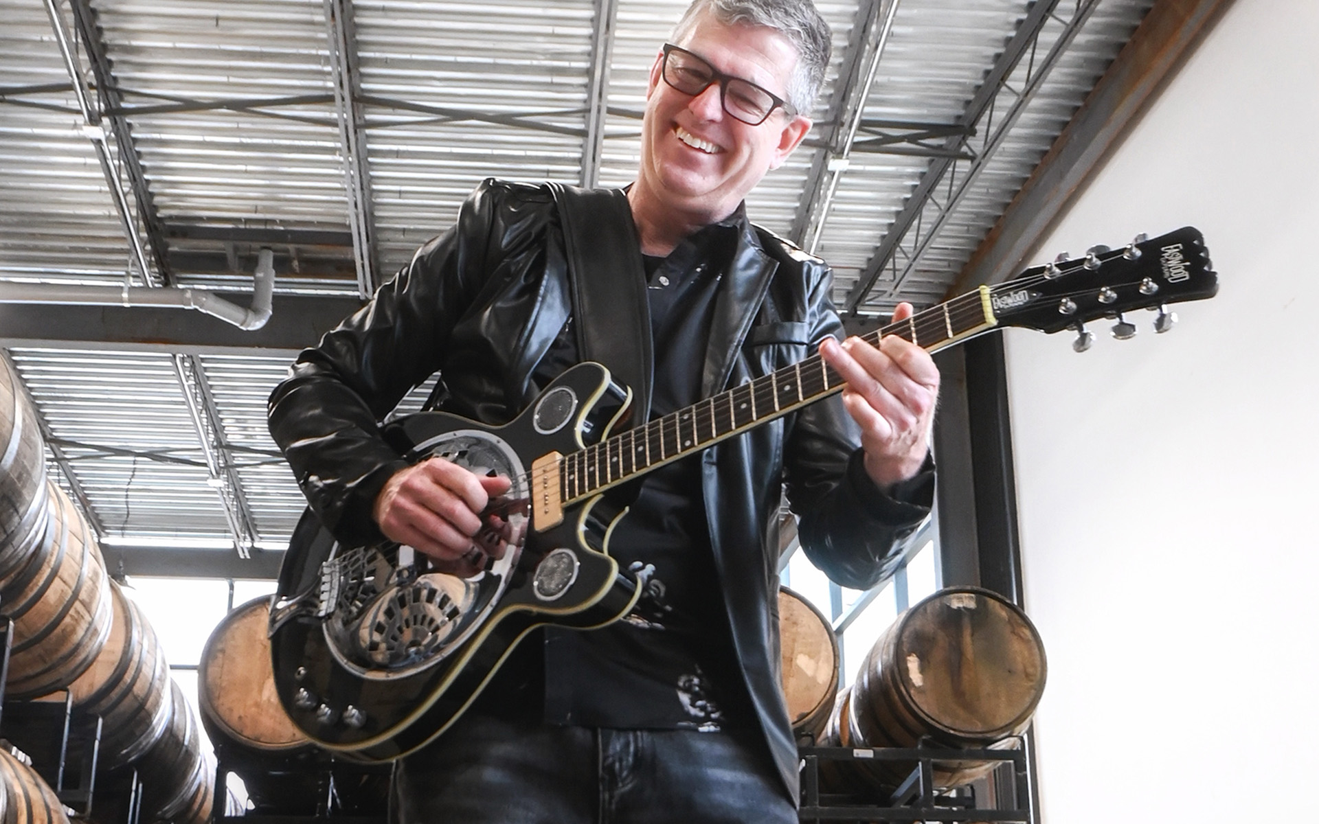 Guitar Performance graduate Bob Corson playing guitar in a warehouse with barrels in the background. 