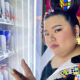 An artistic photo of Ashley Aunor standing in front of a glowing vending machine with rubik's cubes in their hair, on their jacket, and on earrings.