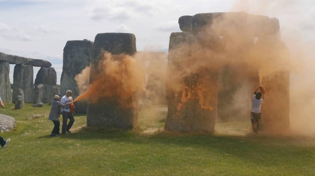 Two protestors spray orange powder paint on the Stonehenge monument.