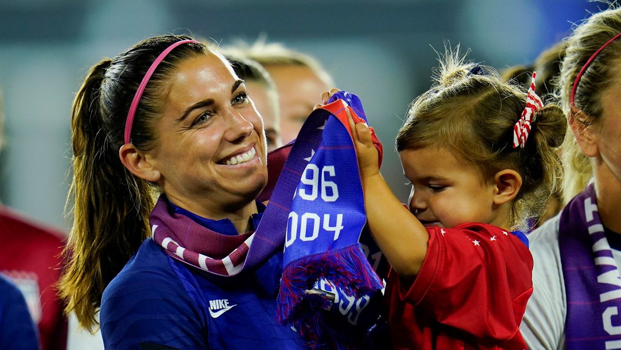 United States' Alex Morgan holds her daughter, Charlie, as she listens to Cindy Parlow Cone, president of the U.S. Soccer Federation, speak during an event with the federation, U.S. Women's National Team Players Association and the U.S. National Soccer Team Players Association at Audi Field in Washington, Tuesday, Sept. 6, 2022. (AP Photo/Julio Cortez)