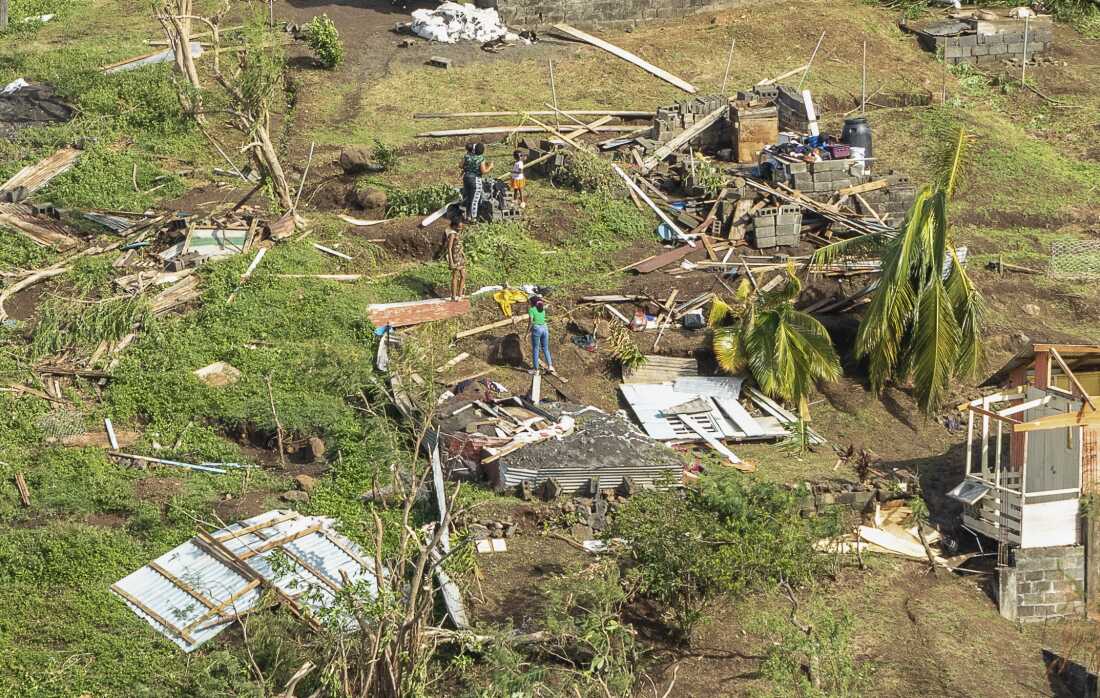 Family members survey the remains of their home in a grassy area.