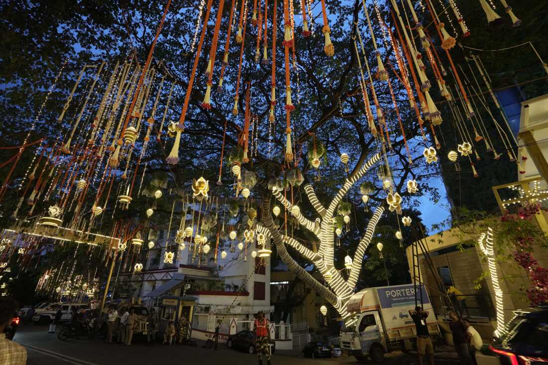 People walk past the Antilia mansion, house of billionaire Mukesh Ambani, while it is lit up ahead of his son Anant Ambani and Radhika Merchant's wedding in Mumbai, India, Wednesday, July 10, 2024. (AP Photo/Rajanish Kakade)