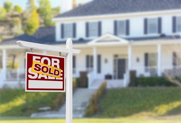 A house with a Sold sign pasted over the top of a For Sale sign in a yard.