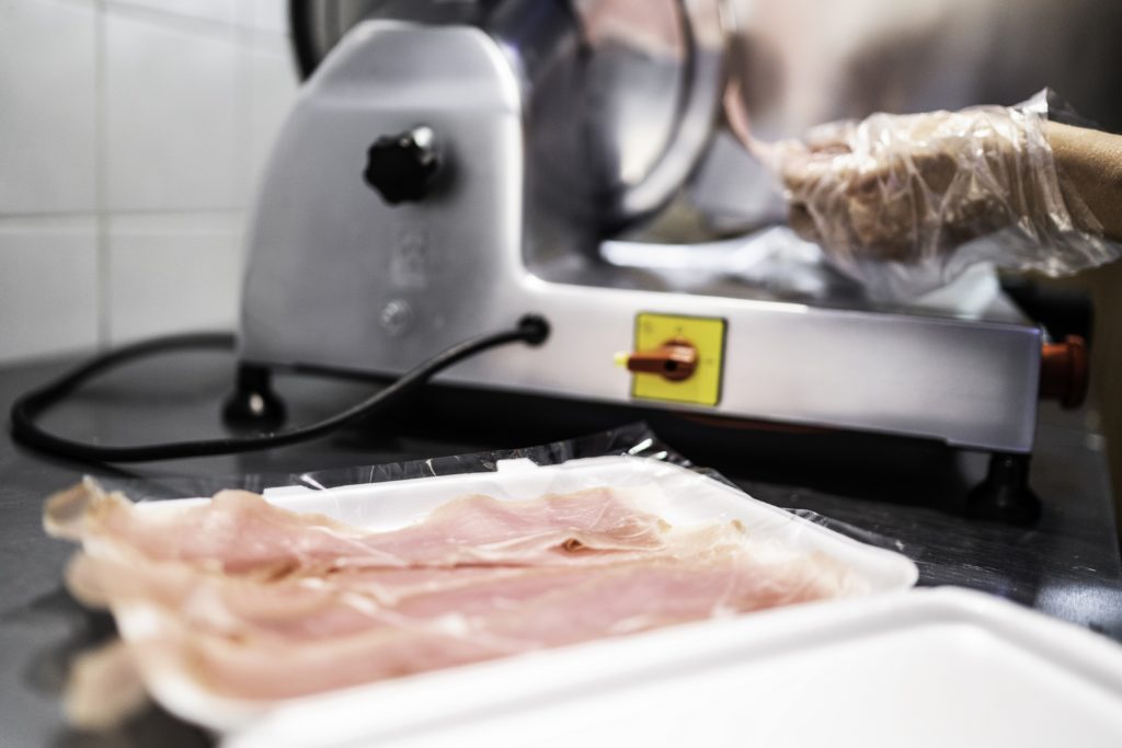 Human hand slicing a piece of ham in the meat slicer