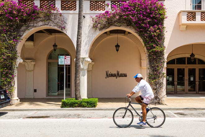 A cyclist rides past Neiman Marcus on Worth Avenue in Palm Beach, April 21, 2020. The parent of Saks Fifth Avenue said it was buying rival Neiman Marcus with the help of Amazon.