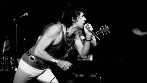 Getty Images English Blues and Rock musician John Mayall performs onstage at Greenwich Village's Bottom Line nightclub, New York, New York, January 23, 1979. Mostly obscured in the background are Ruben Alvarez, on drums, and Harvey Mandel, on guitar. 