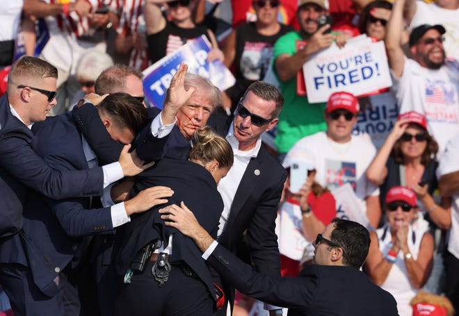 Republican presidential candidate and former U.S. President Donald Trump gestures with a bloodied face while he is assisted by U.S. Secret Service personnel after he was shot in the right ear during a campaign rally at the Butler Farm Show in Butler, Pennsylvania, U.S., July 13, 2024. REUTERS/Brendan McDermid