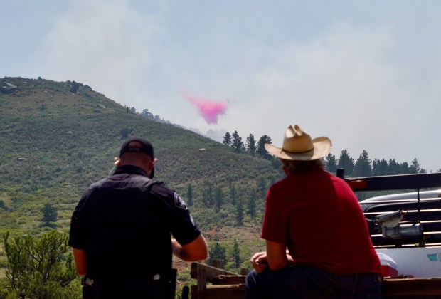 Boulder County sheriff's Sgt. Cody Sears talks to Matthew Lee about his decision to remain in his home and not evacuate despite the incoming Stone Canyon fire near Lyons on Wednesday, July 31, 2024. In the back, a plane drops red slurry near the plume of the fire. (Photo by Zachary Spindler-Krage/The Denver Post)