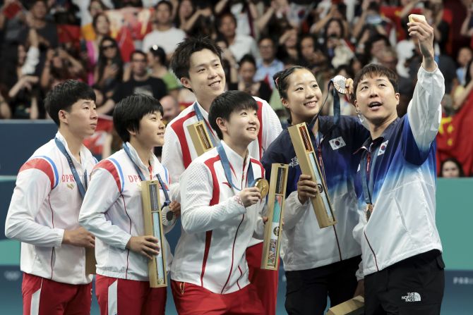 South Korean table tennis player Lim Jong-hoon takes a selfie on the medal podium with his mixed-doubles partner, Shin Yu-bin, and teams from China and North Korea on Tuesday, July 30. Lim and Shin won bronze. On the left is the North Korean team of Ri Jong-sik and Kim Kum-yong, who won the silver. At center is the Chinese team of Wang Chuqin and Sun Yingsha, who won the gold.