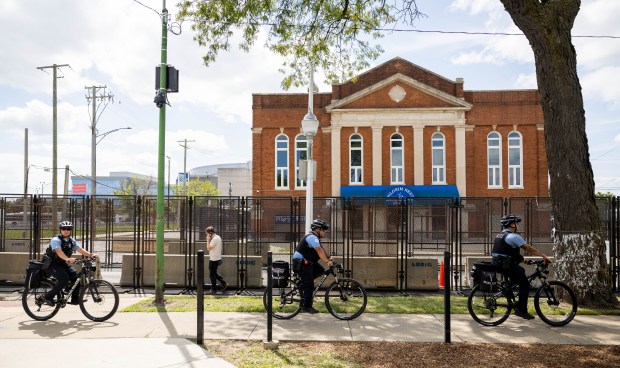 Police officers bike by as activists speak to an empty...