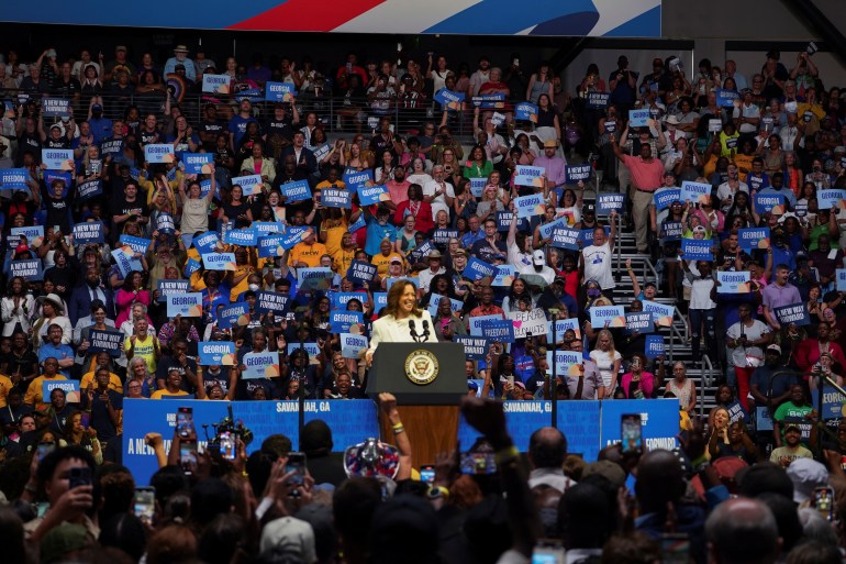 Kamala Harris behind a podium at a crowded campaign rally.