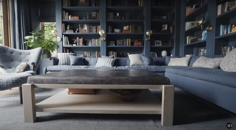 A blue sectional and fuzzy armchair in front of blue built-in bookshelves