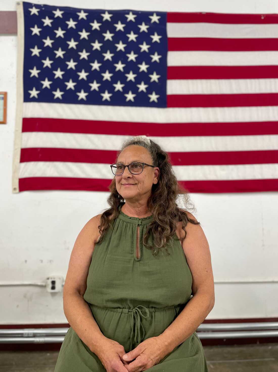 This photo shows Springfield, Ohio, Republican activist Glenda Bailey. She is seated and wearing a green sleeveless dress. An American flag hangs on the wall behind her.