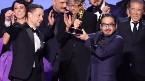 Reuters Shogun's Hiroyuki Sanada holding an Emmy aloft on stage, surrounded by with the show's other stars and makers 