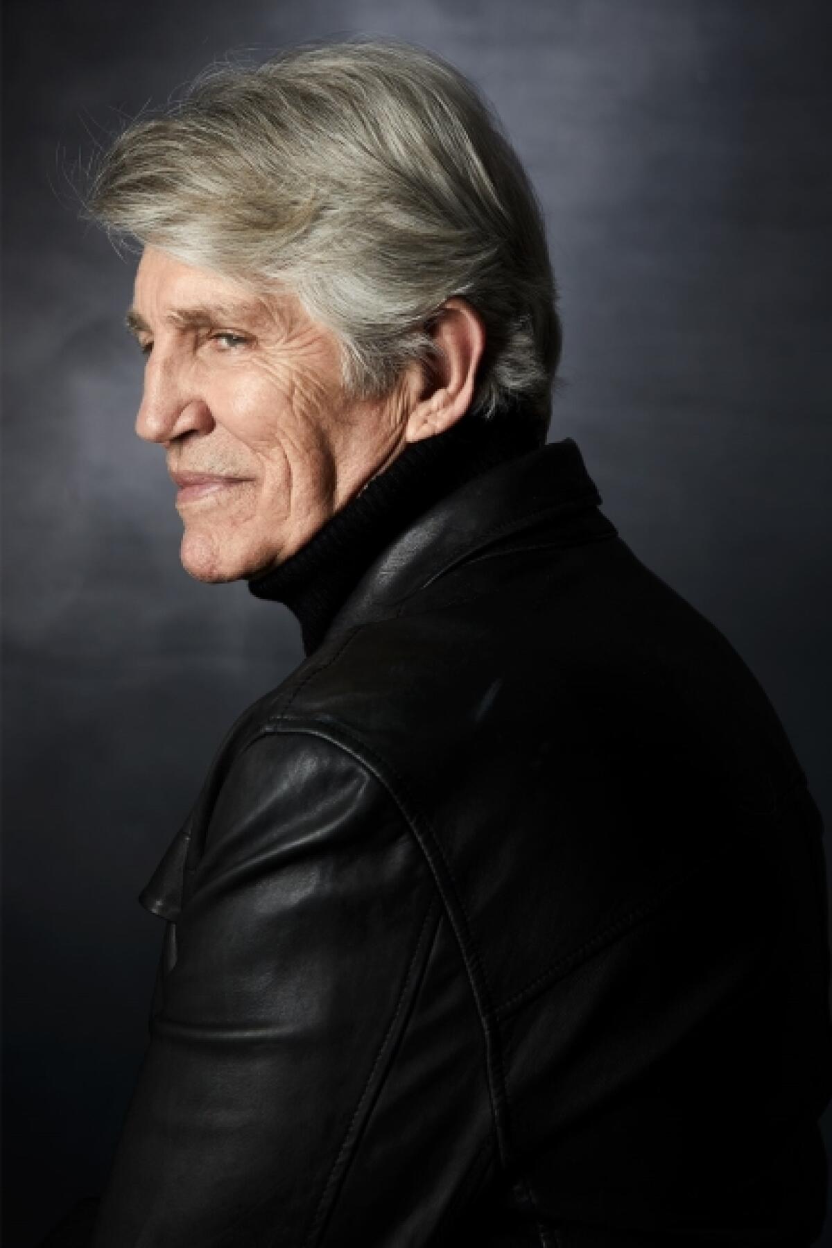 Eric Roberts, in a black turtleneck and leather jacket, is turned to the side.