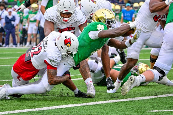 Sep 28, 2024; South Bend, Indiana, USA; Notre Dame Fighting Irish running back Jeremiyah Love (4) stretches the ball across the goal line for a touchdown against Louisville Cardinals safety Tamarion McDonald (12) in the first quarter at Notre Dame Stadium. Mandatory Credit: Matt Cashore-Imagn Images