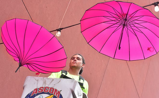 Jose Barajas of Ascom Electric in Dover hangs an umbrella in The Pink Power Parasol Project, which is now hanging in the Cherry Lane Alley behind Central Market in York. About 100 parasols were hung Thursday, September 26, 2024, and will remain there throughout October to bring awareness to Breast Cancer Awareness Month. The North George Street bridge over the Codorus Creek is also decorated. Bil Bowden photo