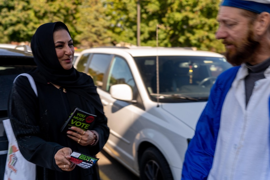 Farah Khan holds a flyer out towards a man who is walking past her.