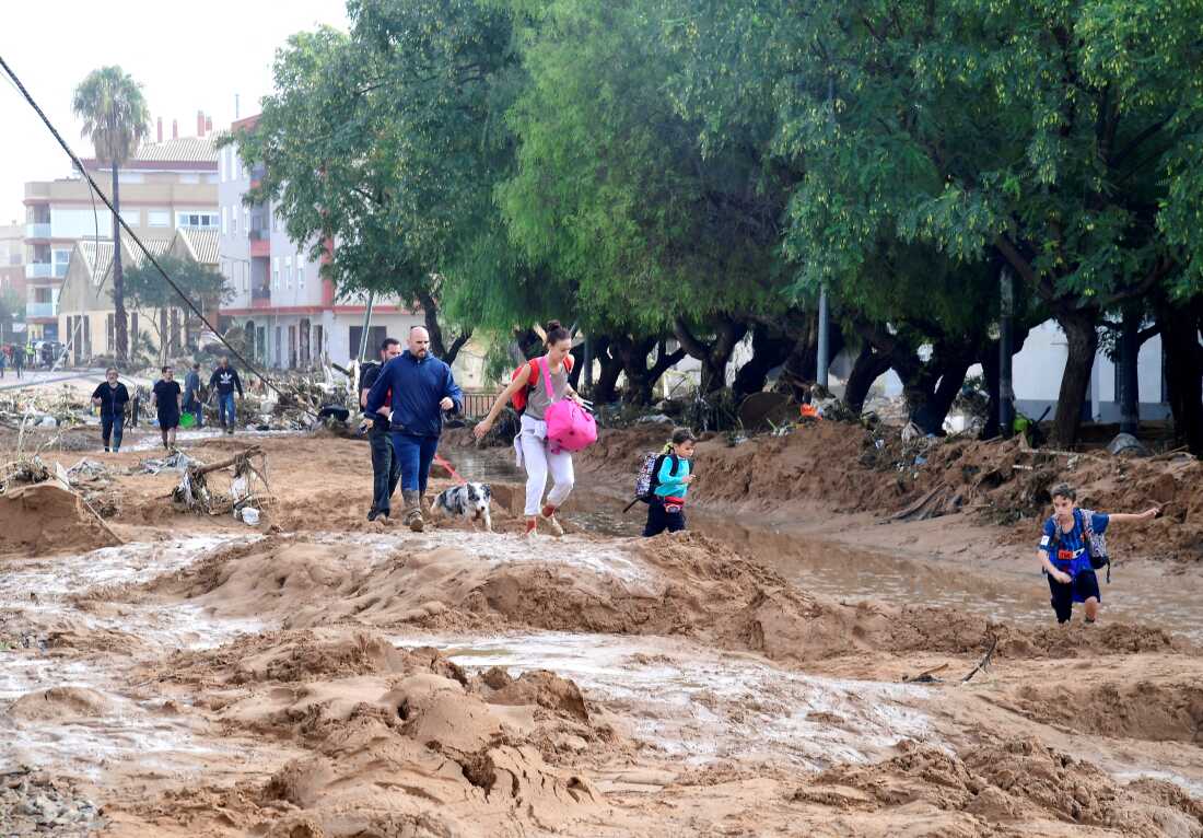 TOPSHOT - Family members walk in a street covered in mud in a flooded area in Picanya, near Valencia, eastern Spain, on October 30, 2024. Floods triggered by torrential rains in Spain's eastern Valencia region has left 51 people dead, rescue services said on October 30. (Photo by Jose Jordan / AFP) (Photo by JOSE JORDAN/AFP via Getty Images)