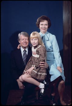 A man in a suit nurses his daughter and sits next to his wife.