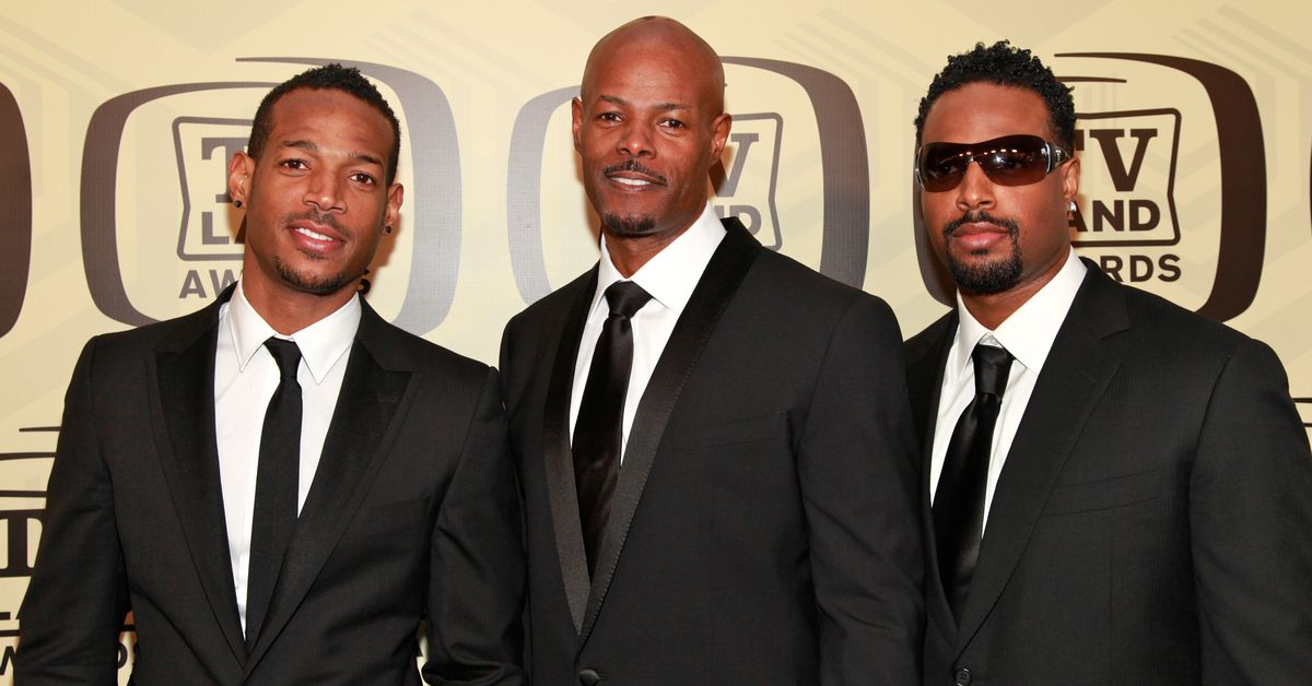 Three men in suits standing in front of a beige backdrop emblazoned with the TV Land Awards logo.