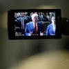 This photo shows former President Donald Trump on a camera monitor as he speaks to the press in February outside Manhattan Criminal Court. He's wearing a blue suit jacket, a red tie and a white shirt. Many people in suits and law enforcement uniforms stand behind him. 