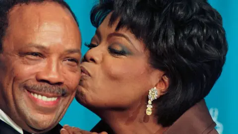 Getty Images Oprah Winfrey kissing a smiling Quincy Jones on the cheek backstage at the 1995 Oscars 