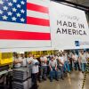 This photo shows factory workers standing on a factory floor. On display is a large sign that says