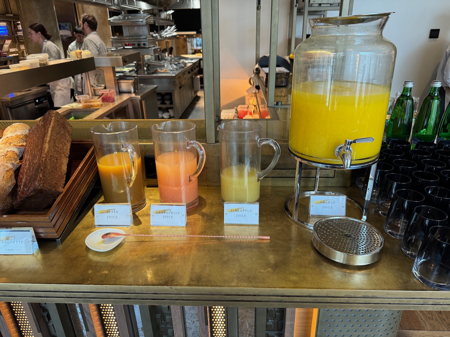 a group of glasses of orange juice and a dispenser on a table