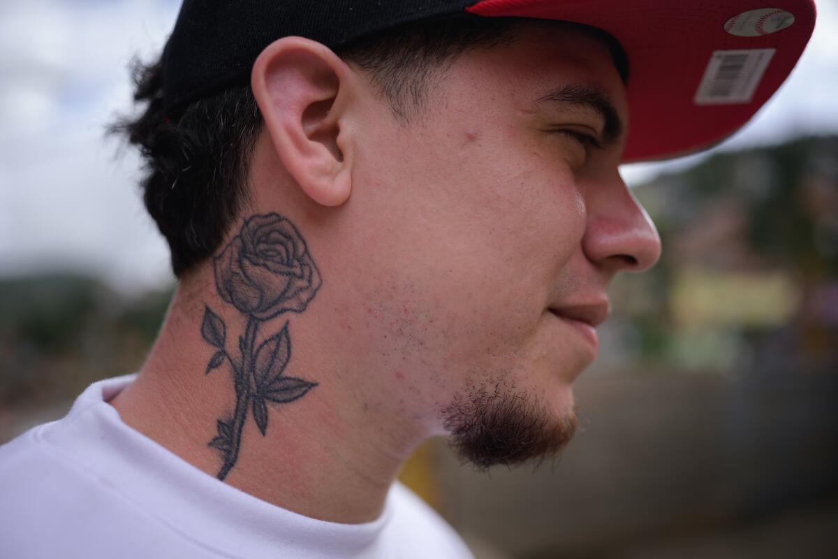 A bearded man in a cap, with a rose tattoo on his neck