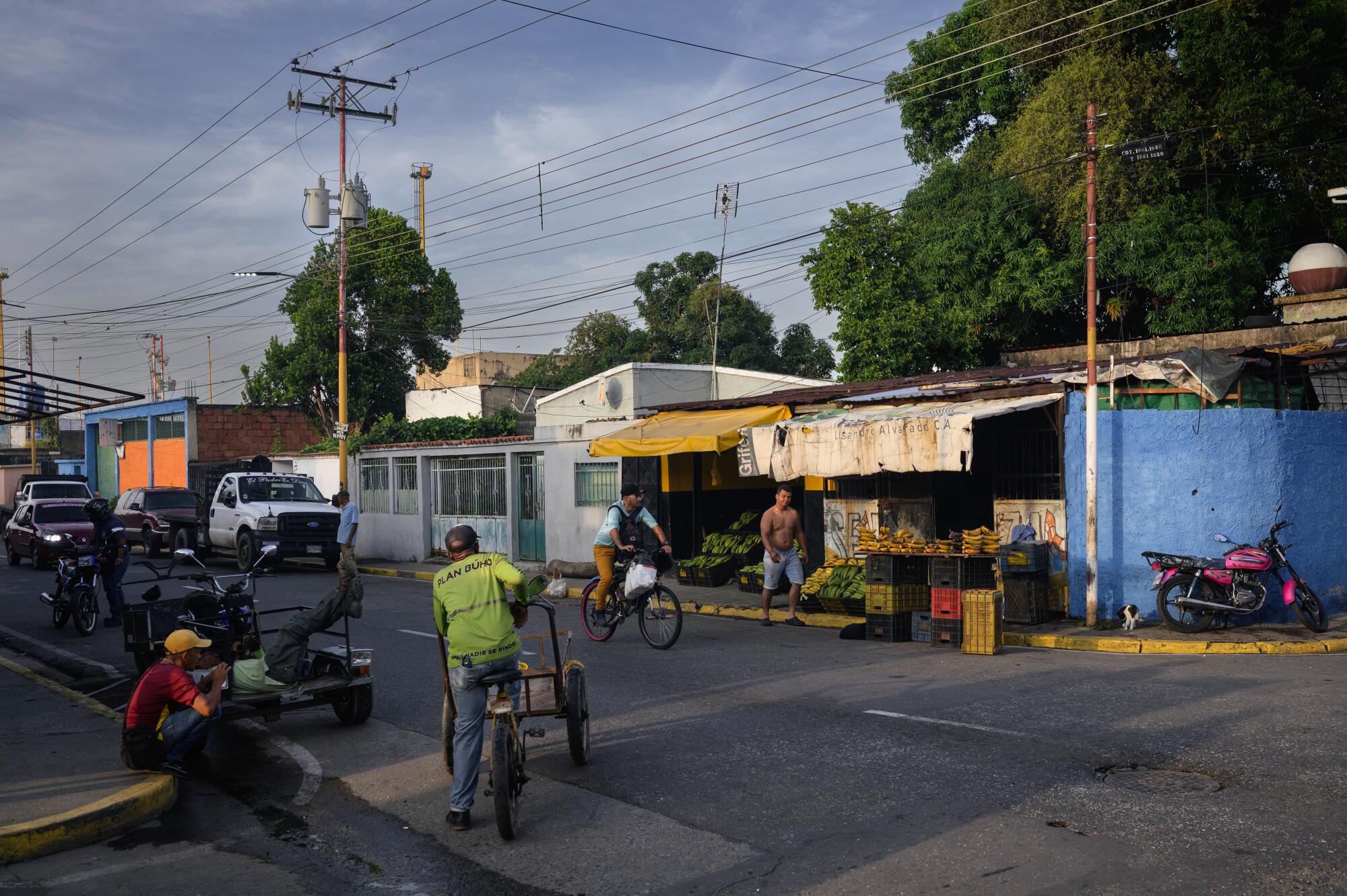 A view of people near vehicles, one riding a bicycle, on a street near buildings