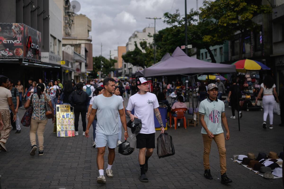 Two men walk near other people. Behind them are buildings