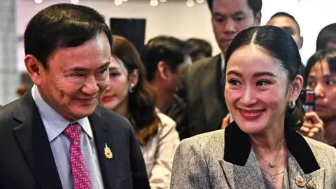 Getty Images Thaksin and Paetongtarn smiling as they stand beside each other, Thaksin wearing a suit and Paetongtarn a grey blazer.