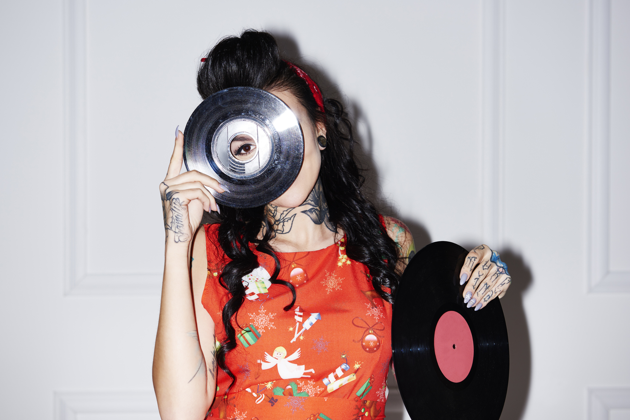 A woman dressed in vintage clothing holds a record over her face, with her eye peering through the record's center hole.