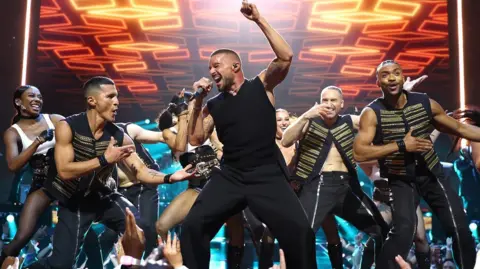 Getty Images Ricky Martin, seen wearing a black vest, performs alongside backing dancers