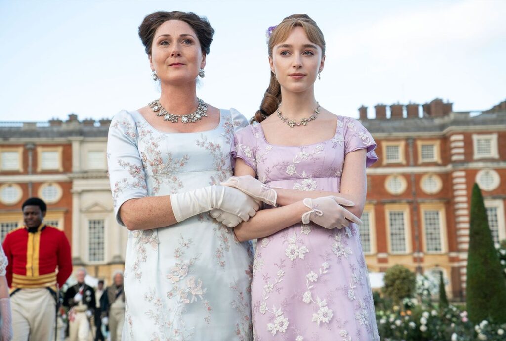 two women walking arm in arm wearing light colored dresses