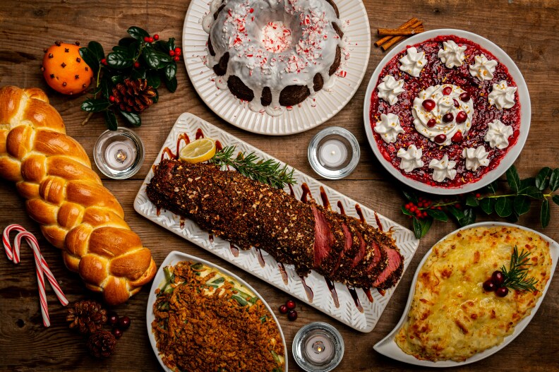 A spread of meat load, baguette, shepherd's pie, baked mac and cheese, a glazed bundt cake, and a floral tart of berries and whipped cream decorate a fall meal at a table.