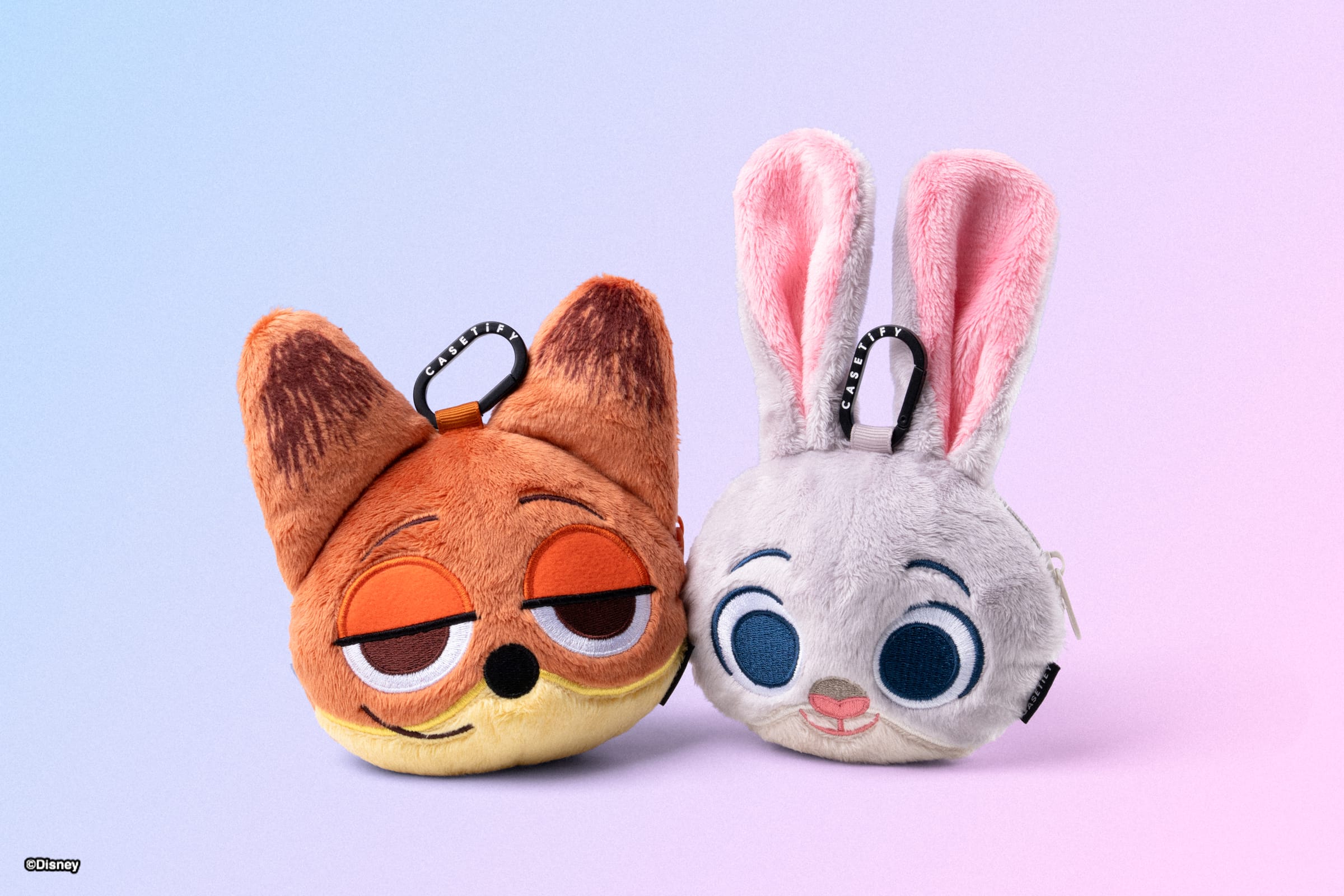 Two plush Zootopia 2 keychains—a fox and rabbit—sit on a pastel gradient, their big eyes as cute as plushies found at Disney parks.