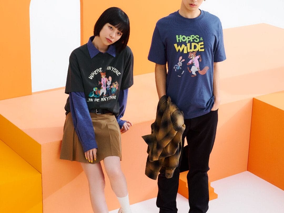 Two young people in Disney Store tees stand relaxed on bold orange and white steps, reminiscent of cheerful Disney park designs.