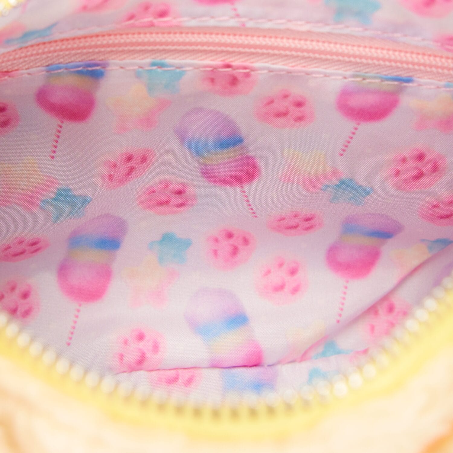 Pastel fabric lining with sweet treats, paw prints, and stars decorates a Disney Store pouch—evoking park magic, no castle shown.