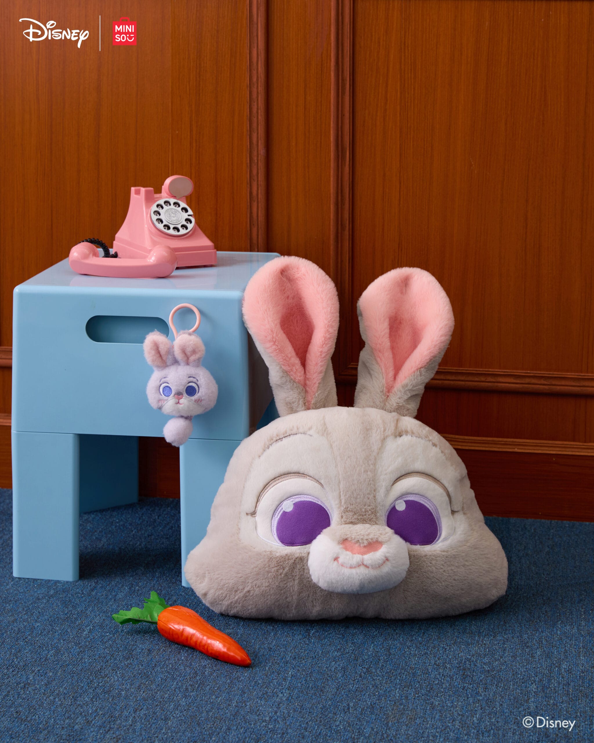 A plush bunny head, carrot toy, and bunny keychain by a blue stool featuring Disney Store and Zootopia 2 items, no castle visible.