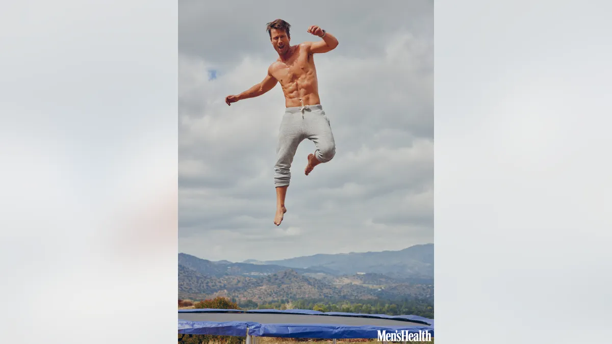 Glen Powell jumping on a trampoline.