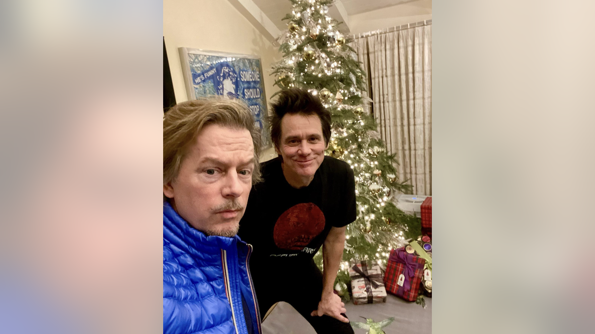 Jim Carrey and David Spade pose in front of a Christmas tree. 