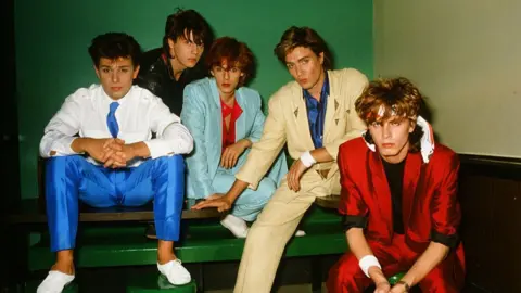 Getty Images British pop group Duran Duran wearing pastel suits of bright red, pale blue, beige, and white a photo studio in Tokyo, Japan in 1982.