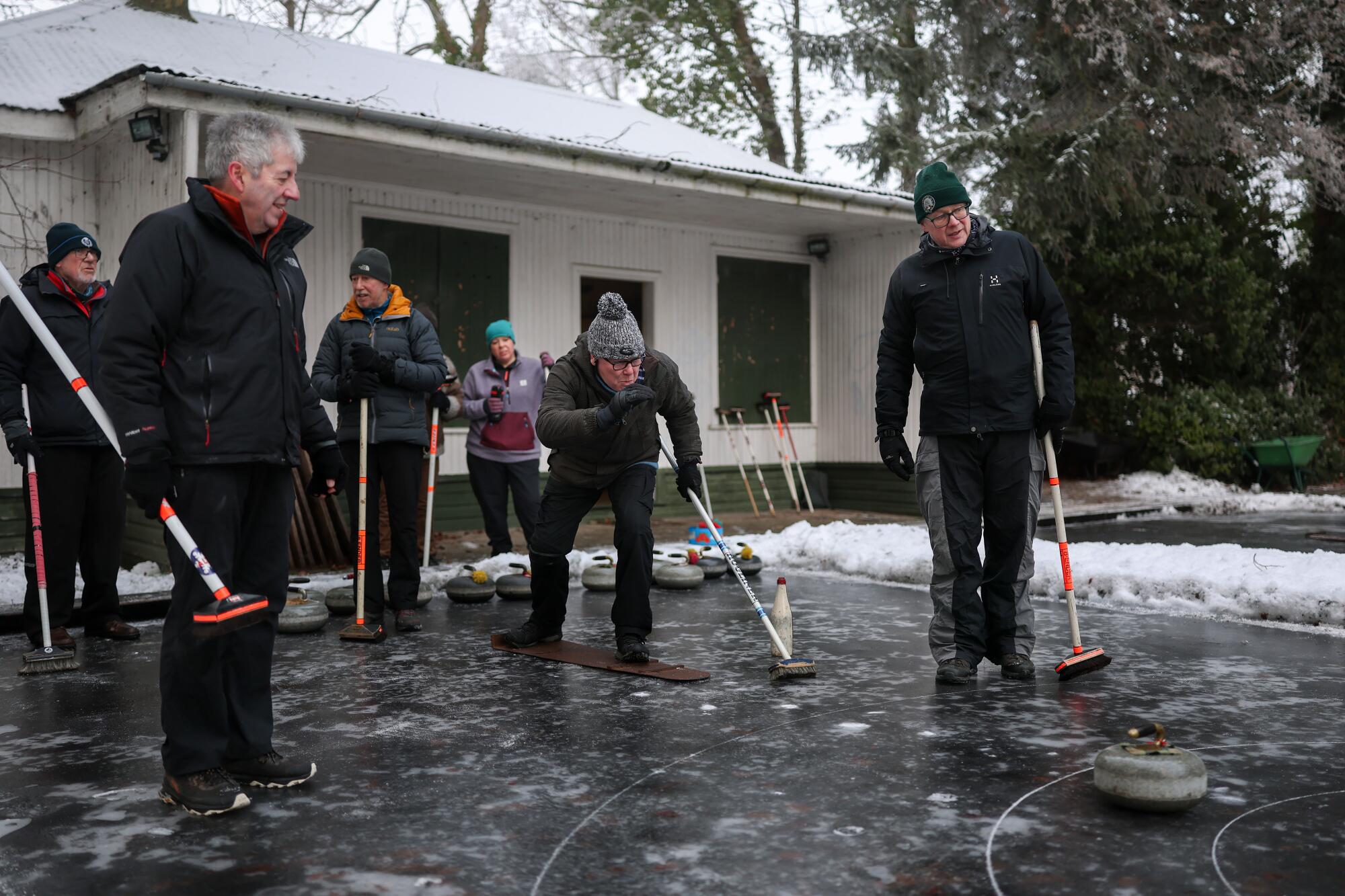 Members of the Highland Curling Club stand on the ice outdoors.