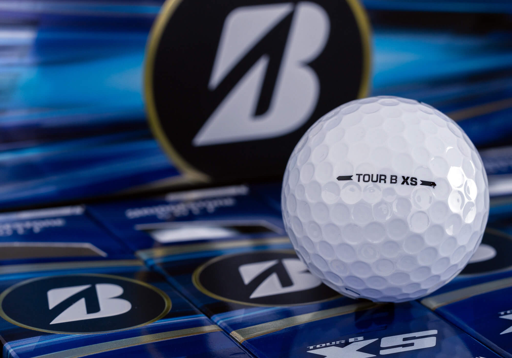 A Bridgestone TOUR B XS golf ball on bright blue packaging.