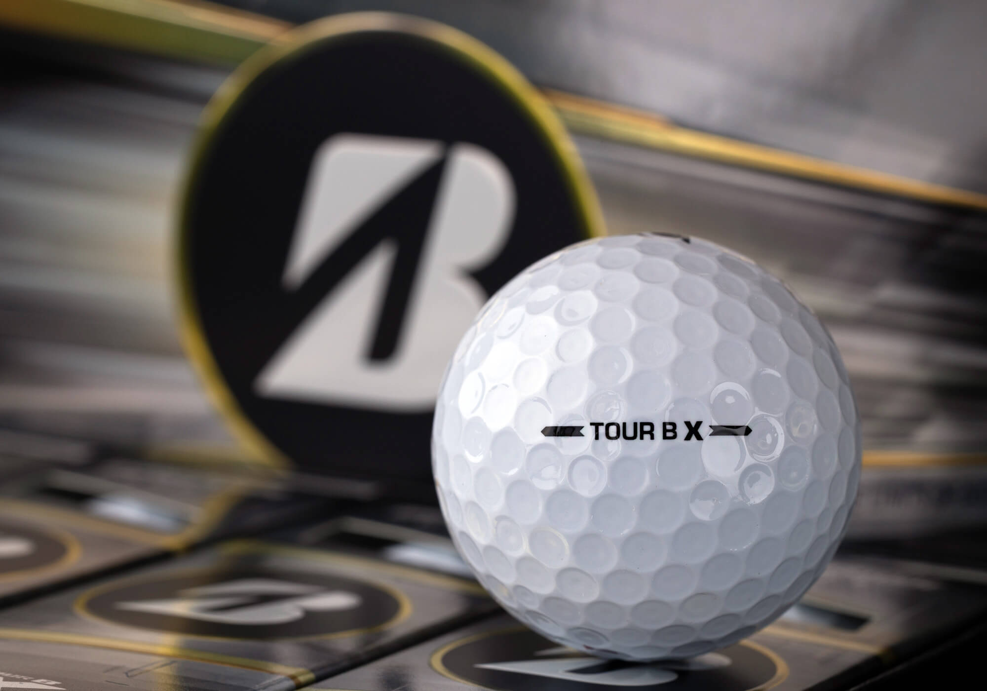 A Bridgestone TOUR B X golf ball on the black and silver packaging