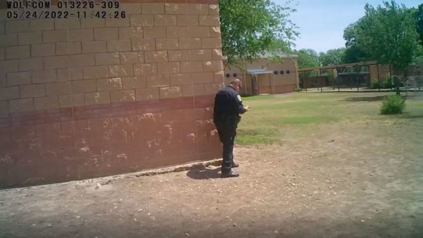 In this still from body camera footage, Adrian Gonzales stands against an exterior corner and uses his radio.