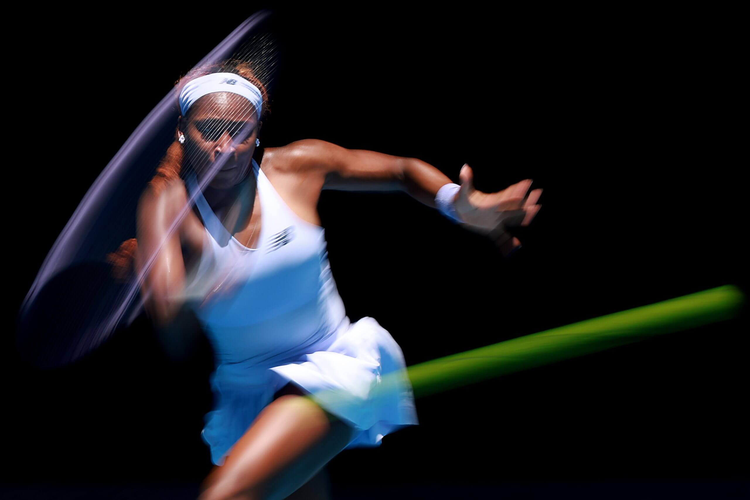 A fast-blur shot of Coco Gauff hitting a tennis forehand.