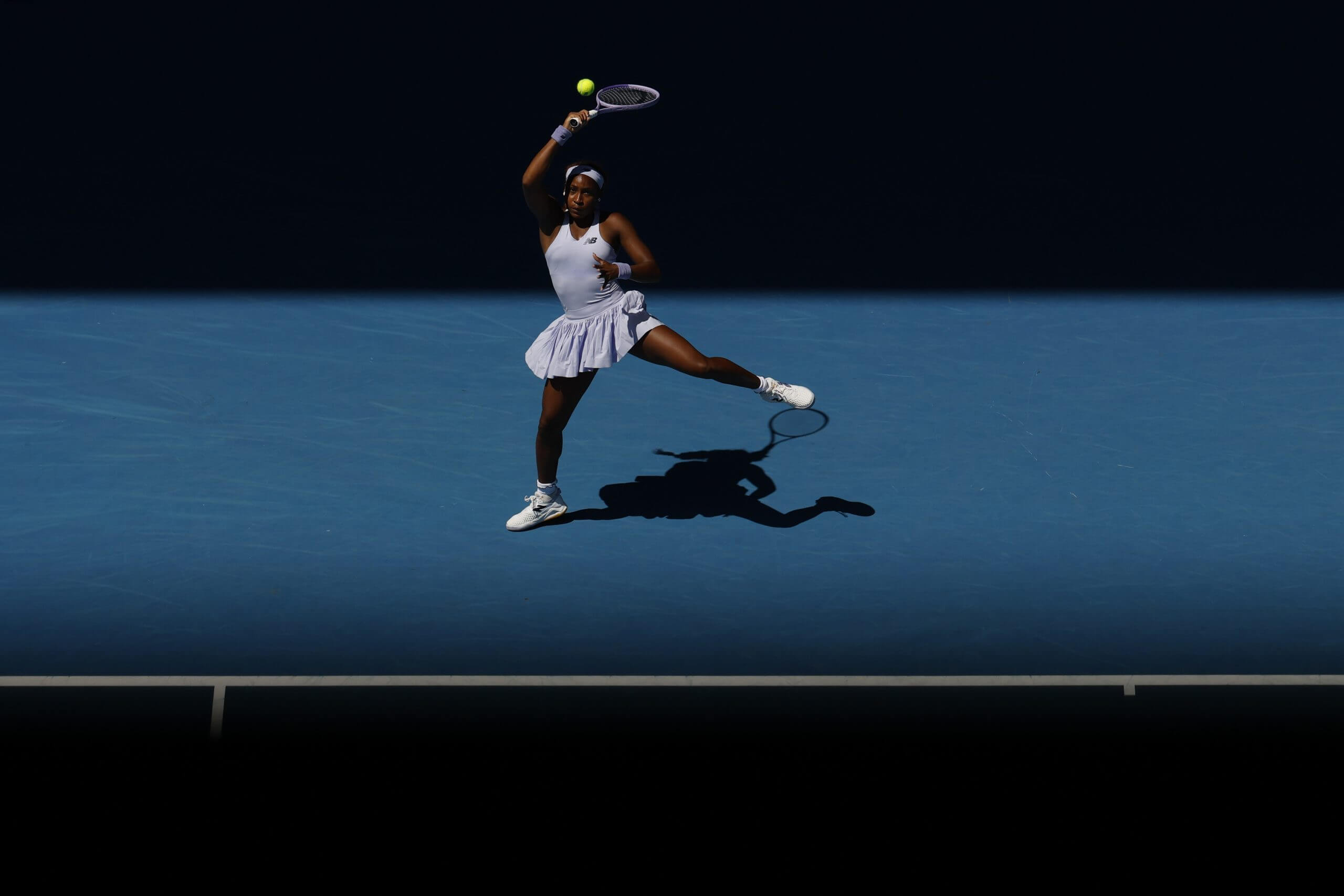 Coco Gauff follows through vertically on a forehand on a blue tennis court.